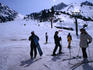 People with skis and snowboards at the bottom of a run on slopes of ski resort.