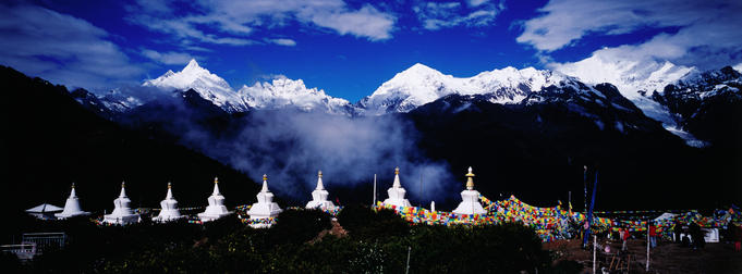 Buddhist stupas and prayer flags with Meili Xueshan mountain range in background.