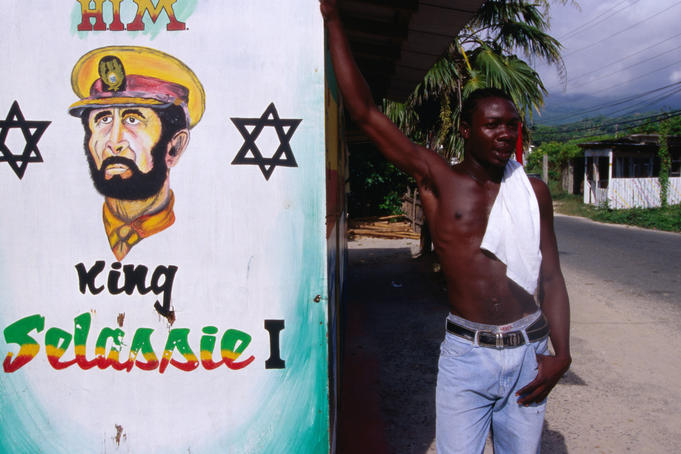 Man standing next to mural of King Selassie I.
