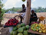Men on bikes behind fruit stand with slash/burn farming in background.