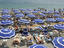 Blue umbrellas and people crowd beach.
