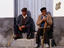 Elderly men with walking sticks sitting in street.
