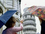 Women with umbrellas looking at Leaning Tower of Pisa.