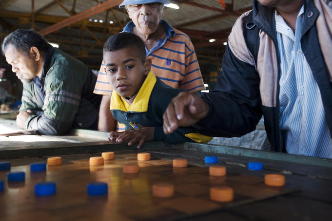 Boy watching men playing draughts.