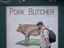 Man walking past pork butcher poster.