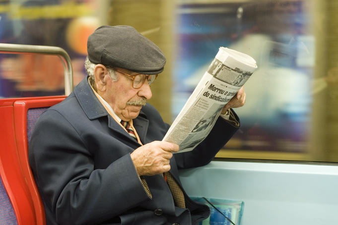 Passenger on subway reading newspaper.