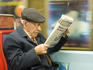 Passenger on subway reading newspaper.