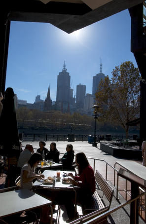 People dining alfresco at Southbank with city high-rises beyond.