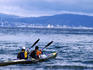 Two people kayaking in Days Bay, with city buildings in distance.