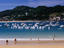 People walking along Playa de la Concha on summer's day with yachts in background.