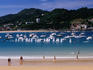 People walking along Playa de la Concha on summer's day with yachts in background.