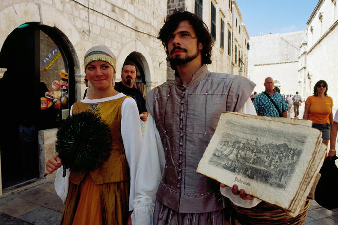 Street entertainers in traditional costume selling souvenirs on Placa in old town.