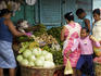 Vendor with customers at vegetable stall next to harbour.