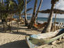 Traditional canoe, palm trees and thatched roof shacks on beach at Miss Elsa's, with couple in background, Little Corn Island.