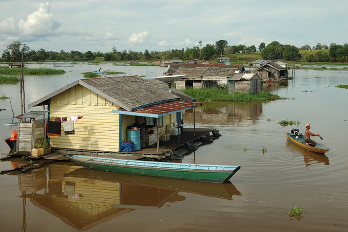 Man on motorised boat near floating houses.