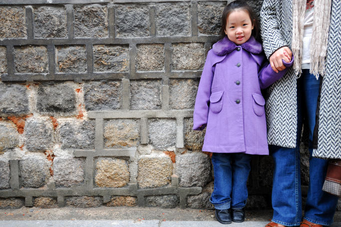 Portrait of young girl standing against stone wall.