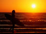Surfer silhouetted against setting sun, Praia do Amado, western coast.