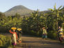 People walking along road with banana plantation and Muhabura volcano behind, Parc National des Volcans.