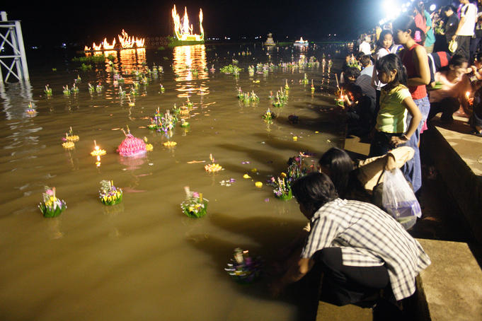 Thai families placing lighted krathong (votive candles & flowers) on Chao Phraya River during Loi Krathong lantern festival at Bangsai Royal Folk Arts and Crafts Centre.