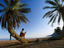 Tourist reading book while sitting on palm tree trunk on beach, Sinai, Red Sea.