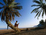 Tourist reading book while sitting on palm tree trunk on beach, Sinai, Red Sea.