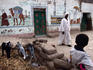 Man, child and baby goats outside house with nicely painted wall, showing that somebody in family has been on pilgrimage to Mecca.