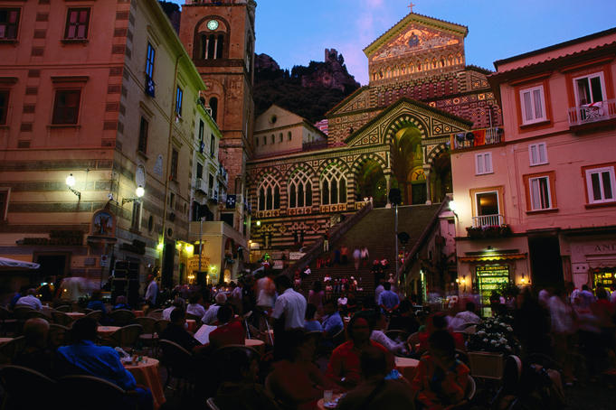 People dining alfresco in front of cathedral at dusk, Costiera Amalfitana.