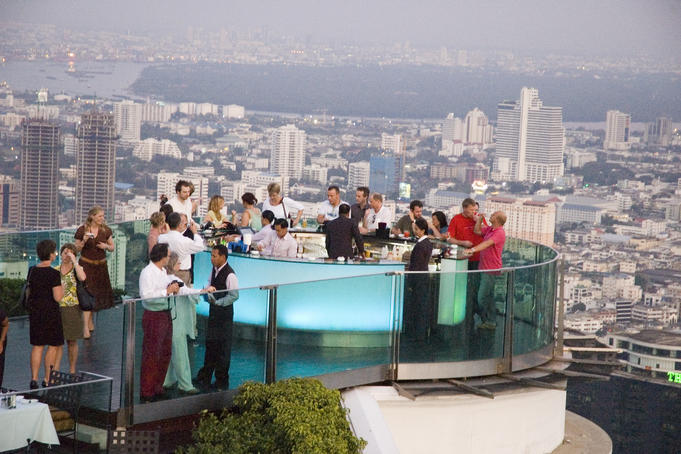 People around circular bar at Sirocco, with city buildings beyond.