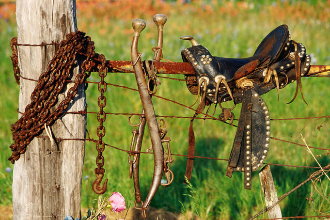 Horse saddle on rusted fence.