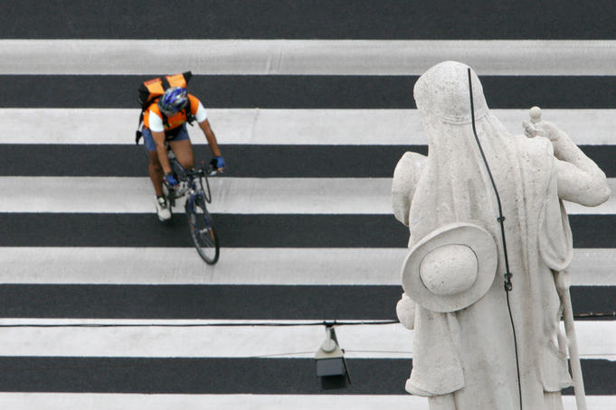 Overhead of cycle courier on a pedestrian crossing under a statue on Szent Istvan Bazilika, Pest.