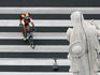 Overhead of cycle courier on a pedestrian crossing under a statue on Szent Istvan Bazilika, Pest.