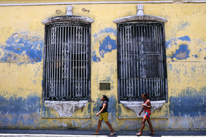 Two women walking past building with barred windows.