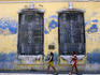 Two women walking past building with barred windows.