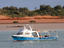 Fishing boat with red earth shoreline in background.