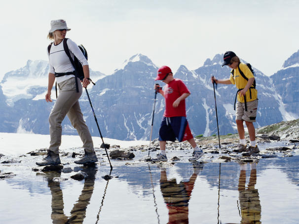 Family crossing alpine creek with mountains in background.