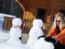 Mother and daughter building snowmen outside chalet.
