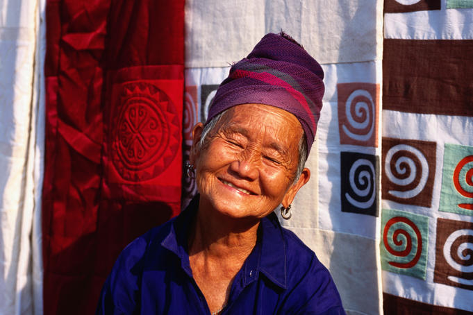 Portrait of Hmong woman at stall with hand made textiles behind.