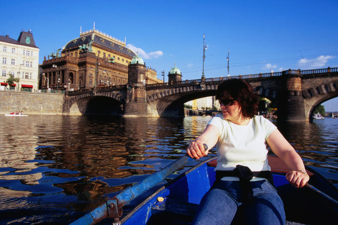 Woman paddling boat on Vltava River near National Theatre.