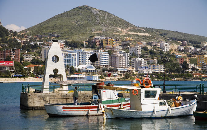 Boats in harbour with high-rise buildings on hill beyond.