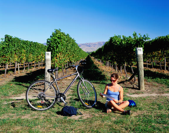 Woman sitting on ground next to her bicycle and checking map with vines behind.