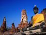 Buddha statue in yellow silk with ruins in background.