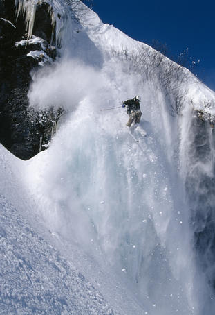 Skier skiing down extreme slope with powder snow falling away.