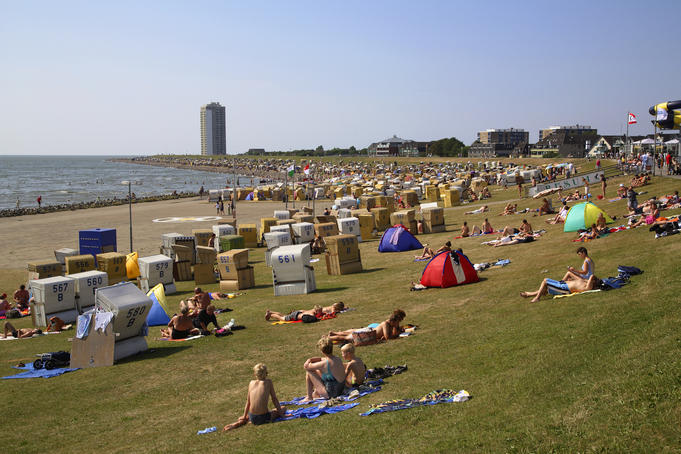 People sunbathing on grass with roofed wicker beach chairs in foreground and North Sea in background, Busum