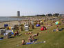 People sunbathing on grass with roofed wicker beach chairs in foreground and North Sea in background, Busum
