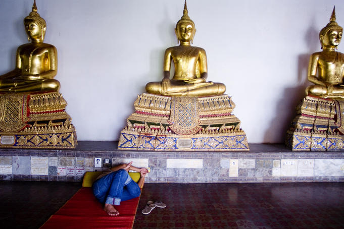 Buddhist statues and sleeping person in temple.