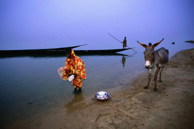 Woman washing dishes by Niger River at dusk.