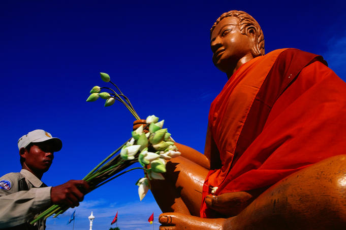 Man with flowers next to Buddha statue.