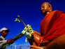 Man with flowers next to Buddha statue.
