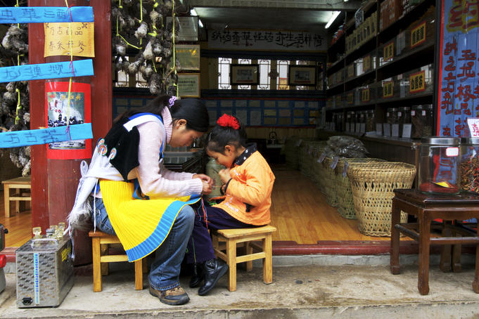Mother and daughter sewing outside a shop.