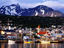 Yachts docked on waterfront, city & mountains.